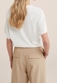 Maglietta a maniche corte bianca in maglia indossata con pantaloni beige a vita alta caratterizzati da due tasche posteriori e un sottile motivo testurizzato.