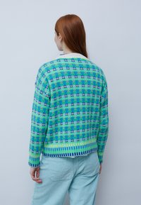Grüner und blauer Strickpullover mit Blumenmuster, gerippten Bündchen und Saum. Verfügt über einen kontrastierenden weißen Kragen und eine lockere Passform.