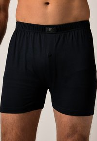 Boxer shorts noirs en tissu doux et extensible. Dotés d'une taille élastique avec une étiquette de logo et d'une fermeture à bouton à l'avant.