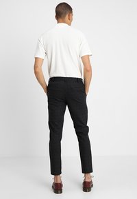 Witte poloshirt voor heren met korte mouwen, gecombineerd met donkergrijze slim-fit broek. Bruine leren schoenen maken de outfit compleet.