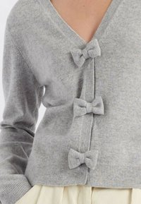 Cardigan grigio con scollo a V, tre decorazioni a fiocco sul davanti e polsini e orlo a coste per un tocco di texture e dettaglio.