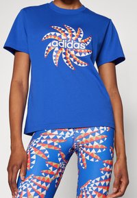 Blå bomulls t-shirt med en grafisk design med orange och vita trianglar samt "adidas"-logga. Matchad med flerfärgade mönstrade leggings.