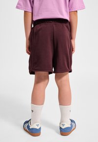 Burgundy bomullsshorts med elastisk midja, sid sömmar och en slät yta, tillsammans med blå sneakers och vita ribbade strumpor.
