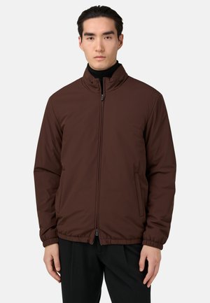 Chaqueta acolchada marrón con cuello alto, cremallera frontal y bolsillos laterales. Presenta puños elásticos y una textura suave.