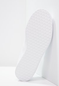 Den vita sneakersulan har en texturerad design med ett hexagonalt mönster. Materialet är gummi som ger grepp och hållbarhet.