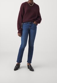 Burgundyröd, fluffig tröja med vida ärmar, i kombination med blå raka jeans. Svarta klackskor med spetsig tå och kraftig klack. Guldig kedjehalsband.