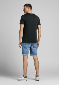 Schwarzes Baumwoll-T-Shirt mit kurzen Ärmeln, kombiniert mit hellblauen Jeansshorts, die an den Säumen aufgerollt sind, und weißen Sneakern mit grauen Akzenten.