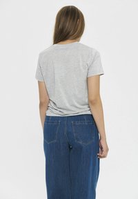 Szary bawełnowy t-shirt z krótkim rękawem, zestawiony z niebieskimi dżinsami o wysokim stanem i szerokich nogawkach, które mają dwie tylne kieszenie i widoczne przeszycia.