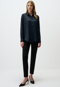 Dark blue long-sleeve shirt with a subtle diamond pattern, button-down front, and a slightly curved hem, paired with black tailored trousers.