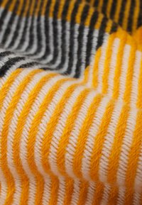 Tecido listrado multicolorido com fios grossos e macios em laranja, branco, cinza e preto, apresentando uma textura ribbed e linhas horizontais proeminentes.