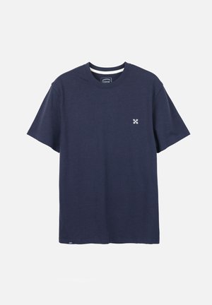 T-shirt bleu marine à manches courtes avec un petit logo blanc sur la poitrine gauche et un col rond sur un fond uni.