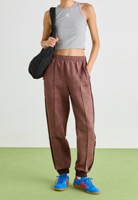 Šedý krátký top, hnědé volné kalhoty s pruhy po stranách a modré sportovní boty s červenými detaily. Černá prošívan á kabelka přes rameno.