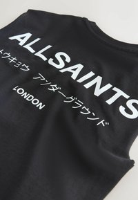 Top negro sin mangas con texto blanco que dice "ALLSAINTS", caracteres japoneses y "LONDON" impreso en el frente.