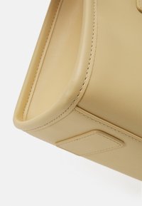 Gul lærveske med glatt tekstur, rektangulær form og synlig søm. Har en flat, firkantet merkelapp på siden.