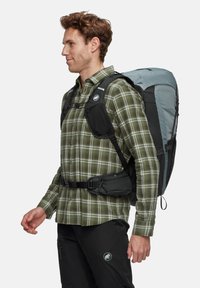 Rucksack mit einem grauen Stoffkörper, Netzakzenten, verstellbaren Trägern und einem schwarzen Hüftgurt. Trägt eine Person in einem grün karierten Hemd.
