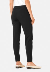 Sorte strækbukser med slim fit, der har en elastisk talje, glat tekstur og tætsiddende ben, parret med lyse slip-on sko.