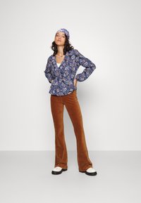 Floral-print wrap blouse in navy blue, paired with brown corduroy flared pants. Finished with white shoes featuring black soles.