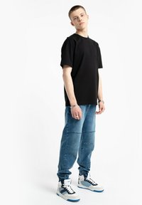 Czarna koszulka z krótkim rękawem zestawiona z niebieskimi dżinsowymi joggerami z detalami w postaci przeszyć oraz białymi trampkami z niebieskimi i szarymi akcentami.