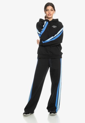 Zwarte hoodie met blauwe strepen op de mouwen, vooraan een kangoeroe pocket, gecombineerd met zwarte joggingbroek met blauwe zijstrepen en een trekkoord.