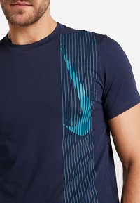 Camiseta de manga corta azul marino hecha de tejido suave, que presenta líneas verticales en color verde azulado de un lado, creando un detalle de diseño elegante.
