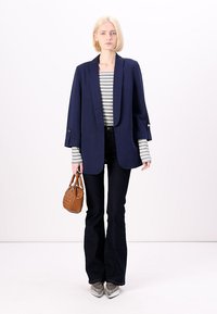 Marinblå kavaj med sjalkrage, randig långärmad topp, mörka utsvängda jeans, silverfärgade spetsiga skor och en brun handväska.