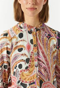 Camicia con colletto caratterizzata da un vivace motivo paisley nei toni del rosa, arancione e nero; chiusura frontale con bottoni e scollatura arricciata in tessuto morbido.