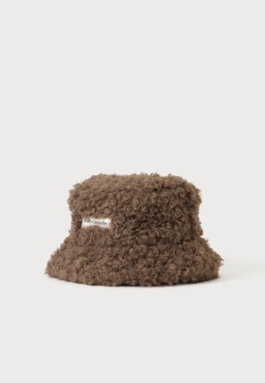 Pruuni lokkis kunstkarvaga kirjakübar, millel on ees "lollys laundry" silt, esitletud ühevärvilise heleda tausta ees.