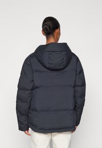 Dark navy puffer jacket with a hood, featuring a quilted design and elastic cuffs. Back view shows ample insulation and a straight hemline.