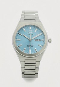 Kvarcinis laikrodis su šviesiai mėlynu ciferblatu, sidabriniais valandų žymekliais ir dienos/data rodmenimis. Nerūdijančio plieno korpusas ir apyrankė su šlifuotu paviršiumi.