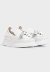 Zapatillas blancas sin cordones con parte superior de cuero perforado, que presentan borlas decorativas y una suela gruesa blanca para mayor altura.