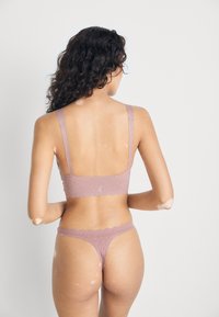 Licht mauve lingerie set met een textuur, geometrisch ontwerp en golvende randen. Inclusief een bralette met brede bandjes en een string ondergoed.