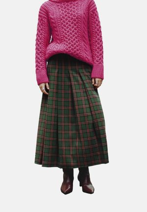 Maglione rosa a lavorazione a maglia con una vestibilità rilassata, abbinato a una lunga gonna verde a quadri con accenti rossi e pieghe, e stivaletti alla caviglia marroni.
