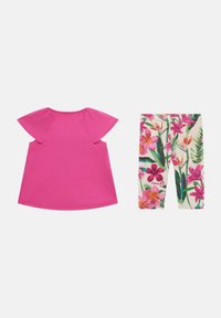 Top rosa a maniche corte con maniche svasate abbinato a leggings floreali con motivi rosa e verdi su uno sfondo chiaro.