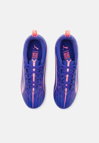 Lila atletiska skor med rosa detaljer, med ett nätövre, snörning och ett strukturerat mönster på sidan.