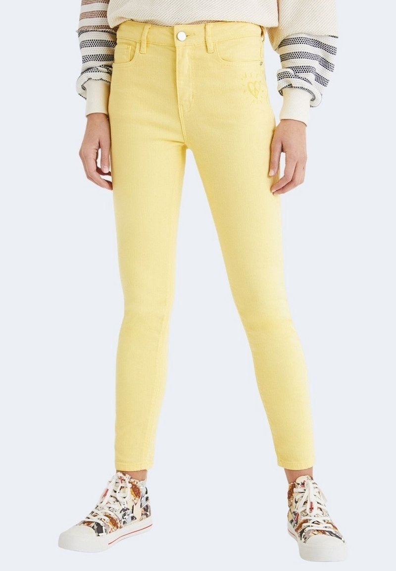 Jean skinny jaune en mélange de coton avec une taille haute. Doté d'une fermeture à bouton et d'une broderie discrète en forme de cœur près de la poche. Associé à des baskets à motifs.