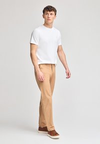 Vit t-shirt med kort ärm, beige byxor, bruna sneakers. Utstyrseln har en enkel design med en logotyp på t-shirten.