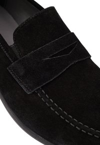 Mocassins en suede noir à semelle plate, dotés d'une sangle repliée décorative et d'une couture ton sur ton le long du bord. Doublure intérieure lisse.