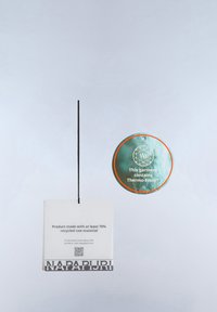 Zwei Kleidungsetiketten hängen vor einem grauen Hintergrund; eines zeigt "Product made with at least 70% recycled raw material,", das andere vermerkt "This garment contains Thermo-Fibre."