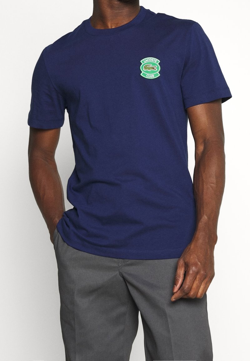 Navy t-shirt made of cotton, featuring a green Lacoste logo badge on the left chest. Short sleeves and a classic crew neck design.