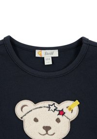 Navyblaue Baumwollt-shirt mit einem gestickten Bärenkopf, der eine strukturierte cremefarbene Felloptik und ein gelbes Stern-Haarband trägt. Größenlabel enthalten.