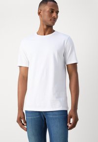 White cotton t-shirt with short sleeves, round neckline, subtle logo on chest, paired with blue jeans. Smooth texture, simple design.