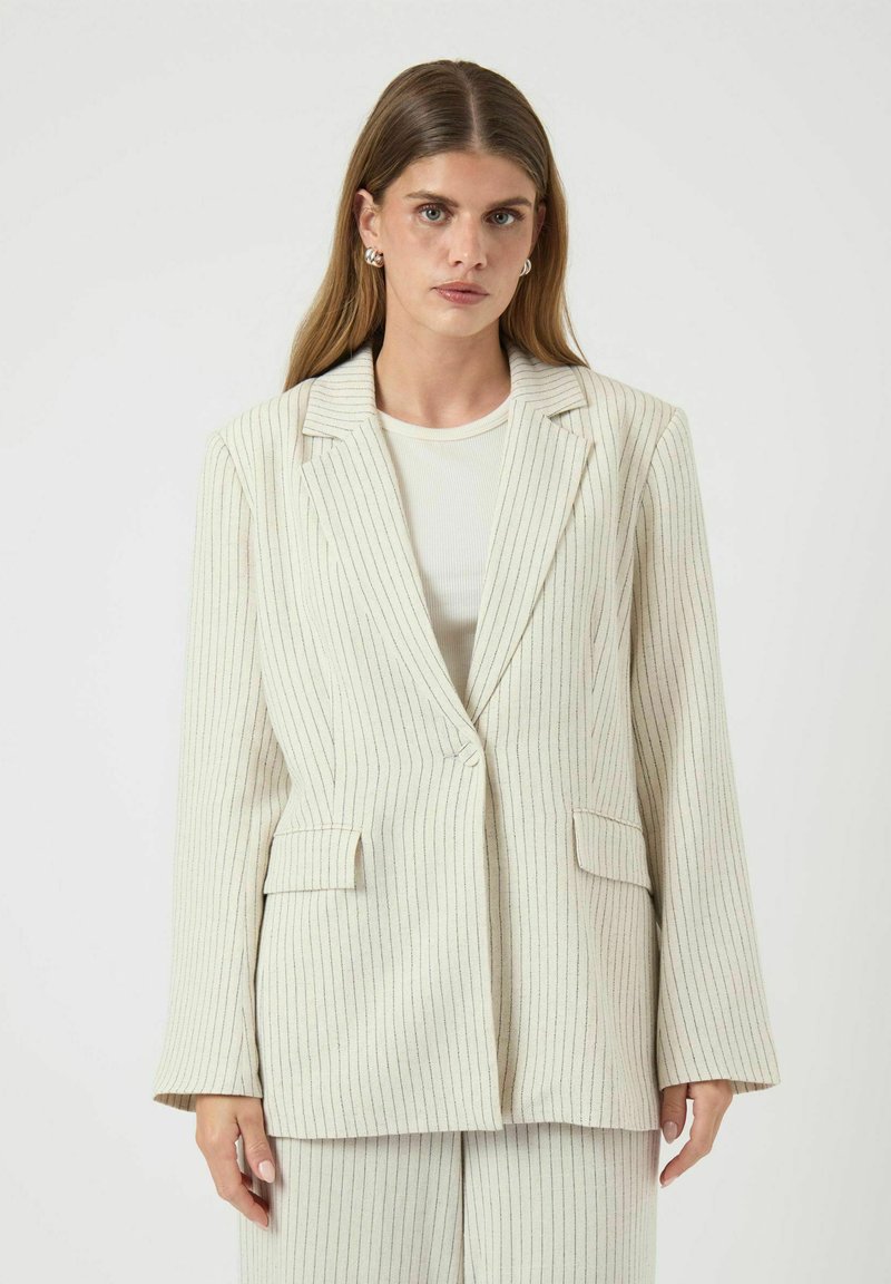 Blazer rayé en crème avec des lignes verticales de couleurs subtiles. Il présente un col cranté, deux poches avant et une fermeture à un bouton.