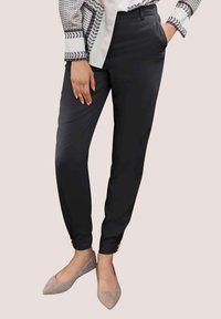 Zwarte op maat gemaakte broek met zijzakken, een gladde textuur, taps toelopende pijpen en gouden knoopaccenten bij de manchetten, gecombineerd met beige puntige ballerina's.