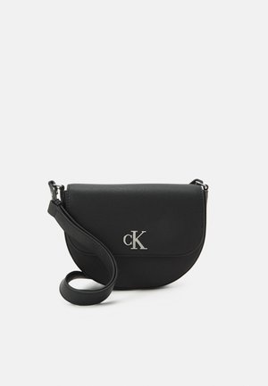 Sac bandoulière noir semi-circulaire avec sangle réglable et logo argenté "cK" sur le rabat avant sur fond blanc.