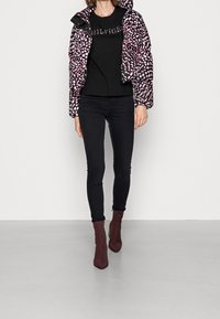 Chaqueta acolchada en patrón rosa y negro, top negro con logo, jeans skinny negros y botas de tobillo puntiagudas en color burdeos. Texturas suaves y diseño ajustado.