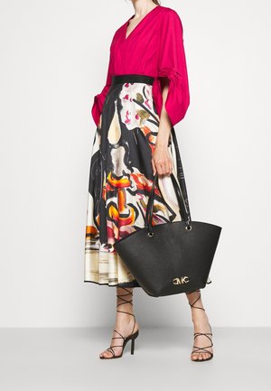 Black leather tote bag with gold logo, paired with a bright fuchsia top with puffed sleeves and a patterned midi skirt featuring bold colors.