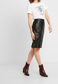 Witte t-shirt met marineblauwe grafische print, zwarte leren kokerrok en bordeauxkleurige krokodillen-embossed enkellaarsjes met een chunky hak.