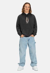 Sudadera negra con un diseño gráfico de llamas en el pecho, combinada con jeans baggy de un azul claro y zapatillas blancas. Tejido suave, ajuste casual.