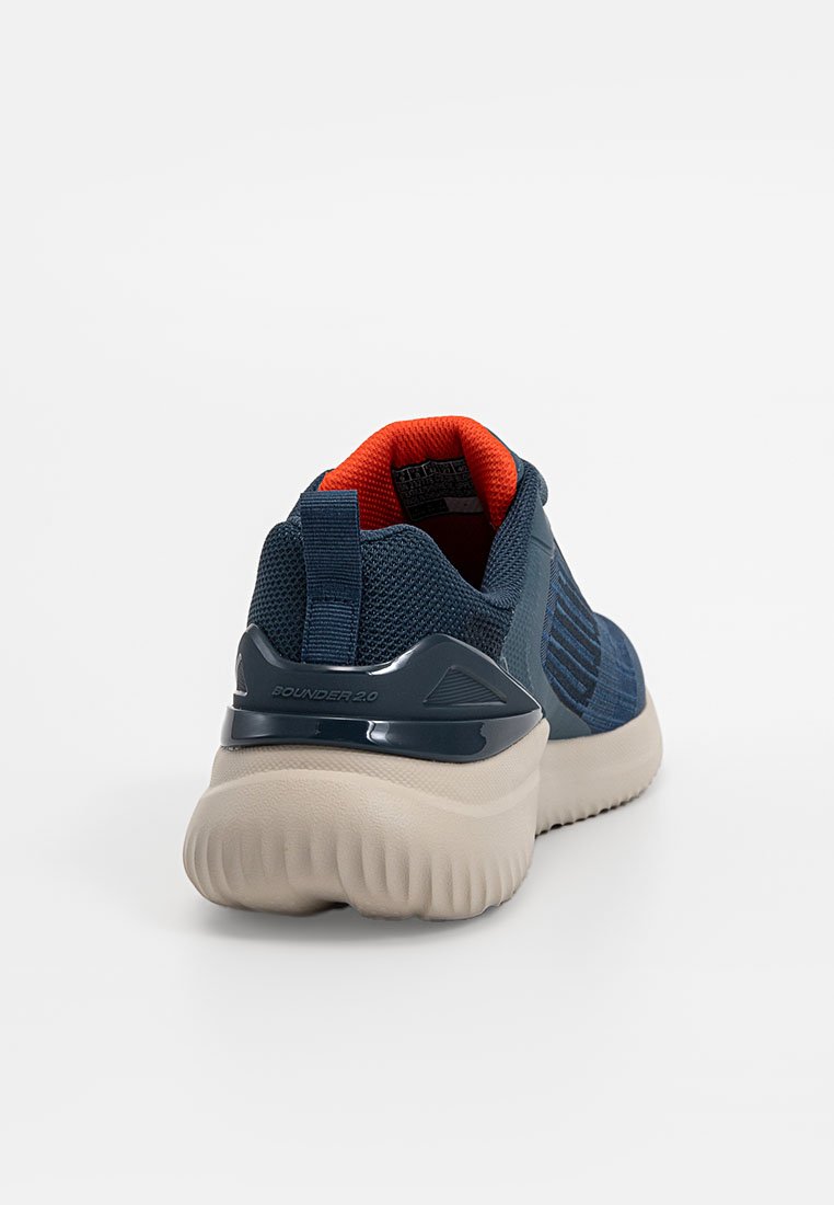 Zapatilla deportiva azul y beige con suela texturizada, empeine de malla, tira en el talón y forro interior naranja, vista desde atrás.