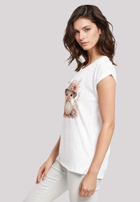 White cotton t-shirt with a rounded neckline, rolled sleeves, and a printed graphic of a cute animal wearing a hat and flowers.